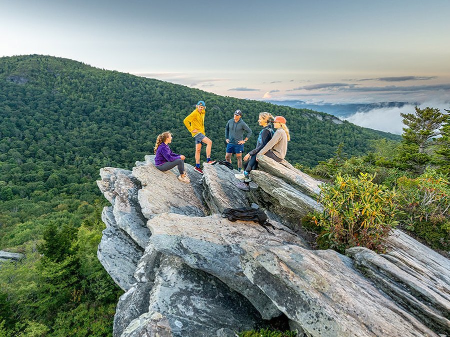 Five hikers resting on a rocky cliff edge above a mountain range
