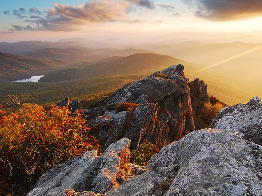 A rocky mountain summit at golden hour above forested ridges