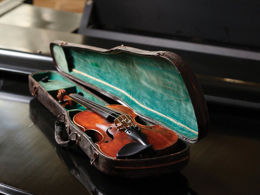 A violin resting in its open case on top of a piano